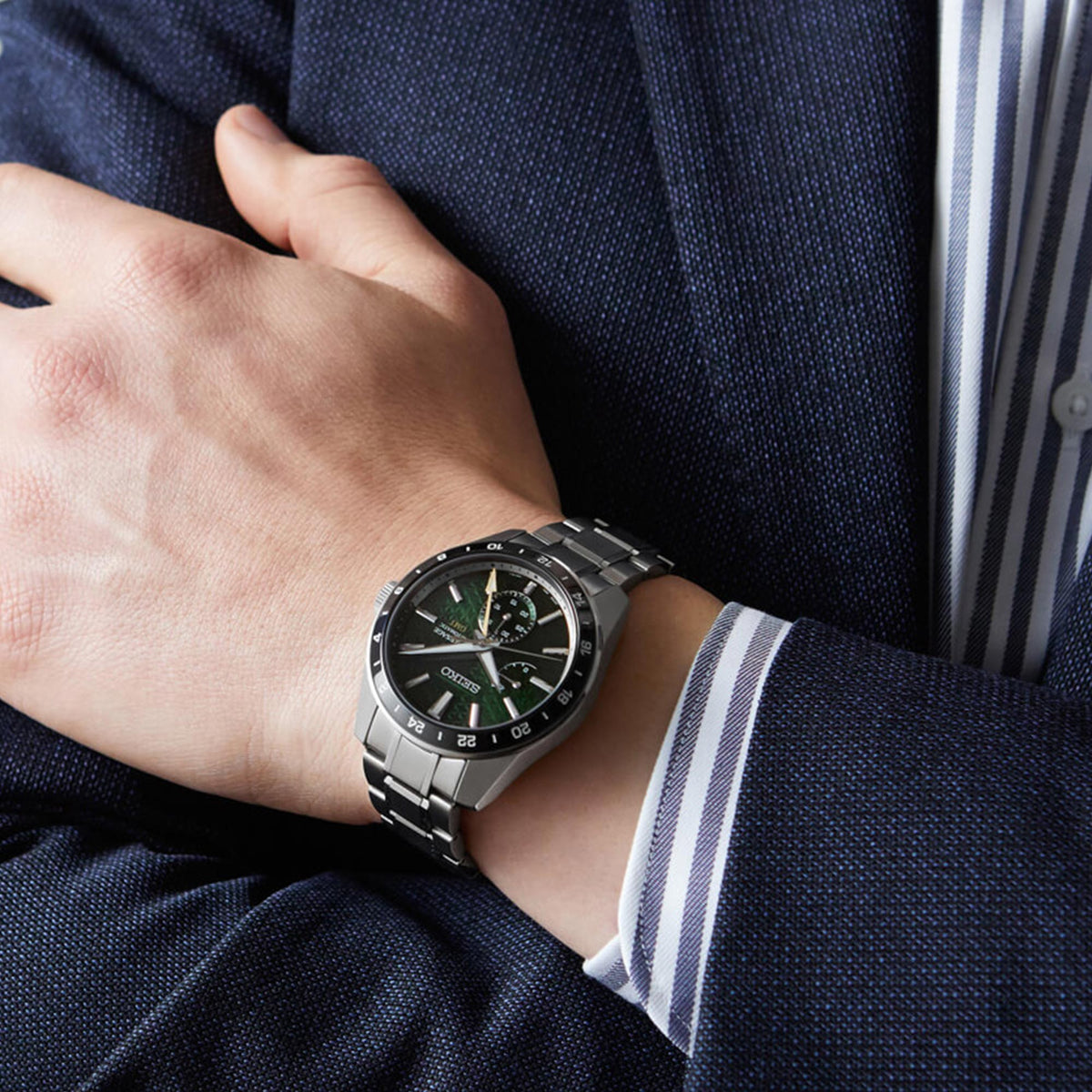 Green dial GMT watch on wrist, silver metal bracelet and black bezel