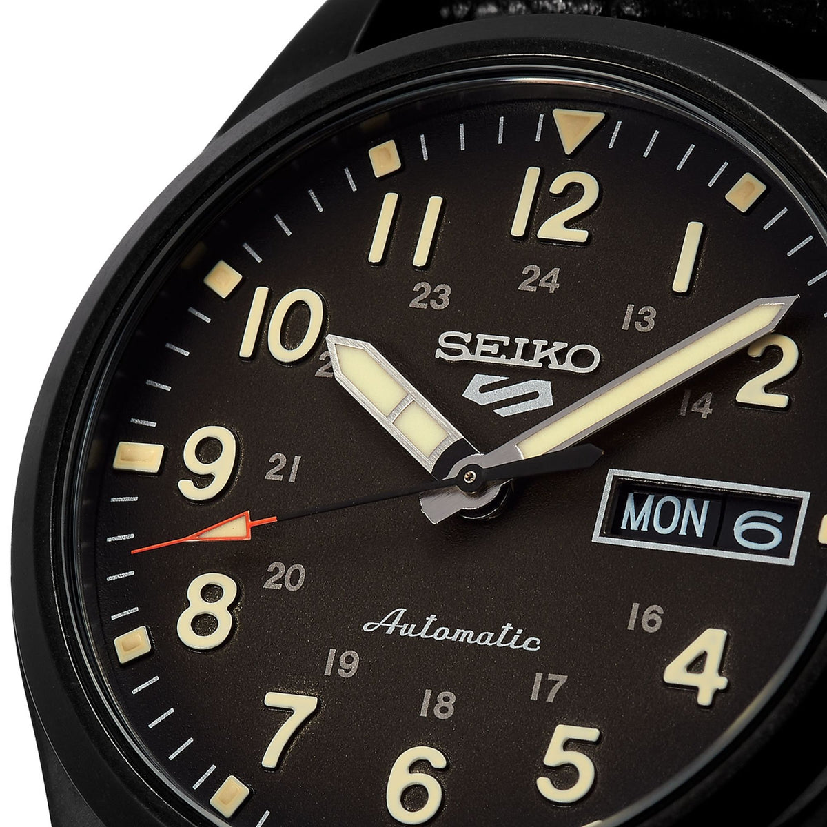 Black dial field watch close-up with SEIKO logo, 'Automatic' text, Arabic numerals, day-date box