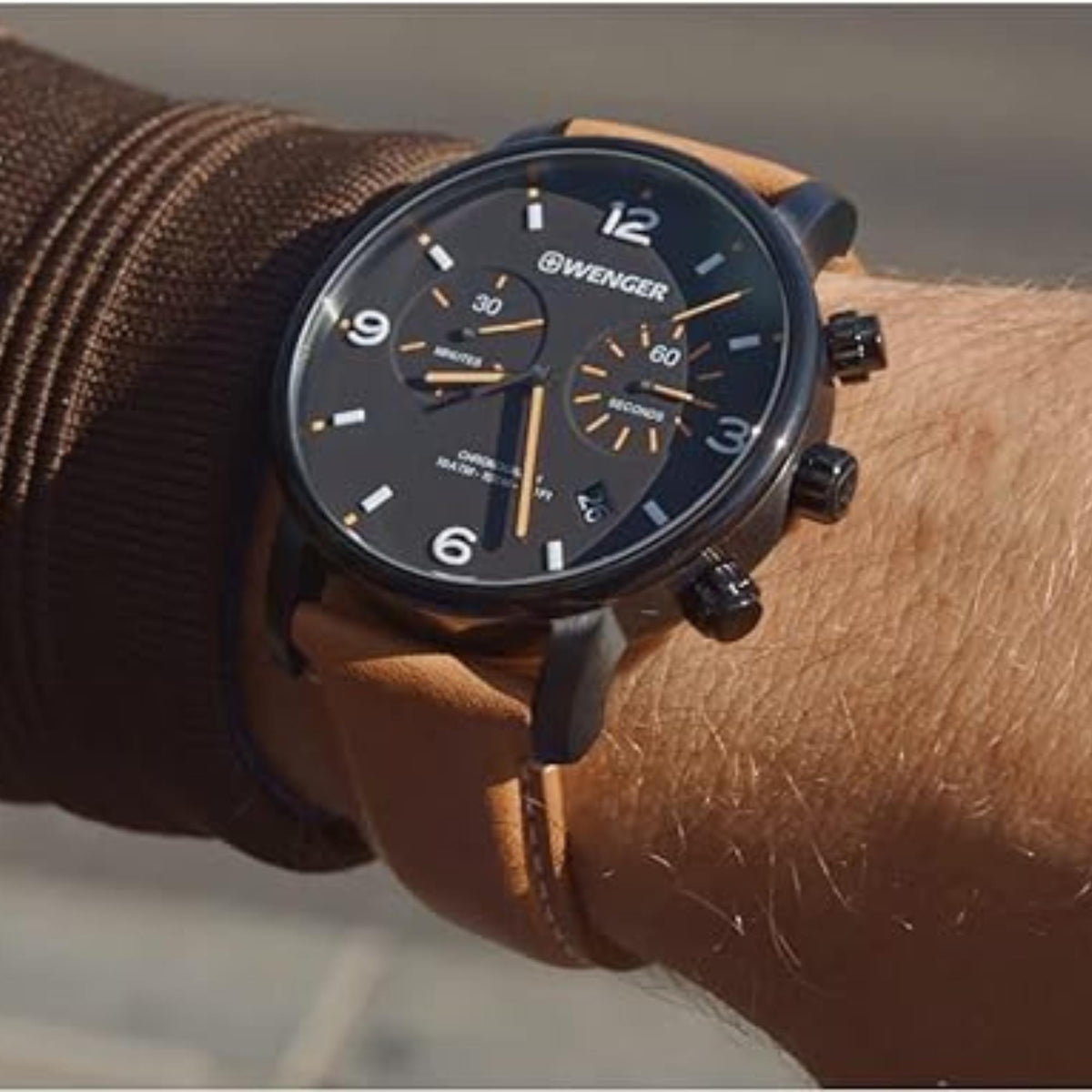 Wenger chronograph watch on wrist, black dial with orange accents and brown leather strap