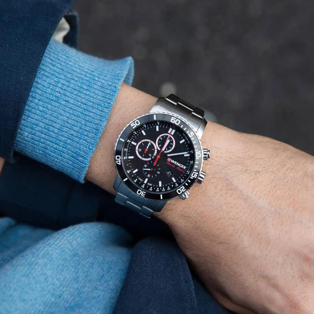 Men's quartz watch with black dial and silver bracelet worn on wrist under a blue sleeve.