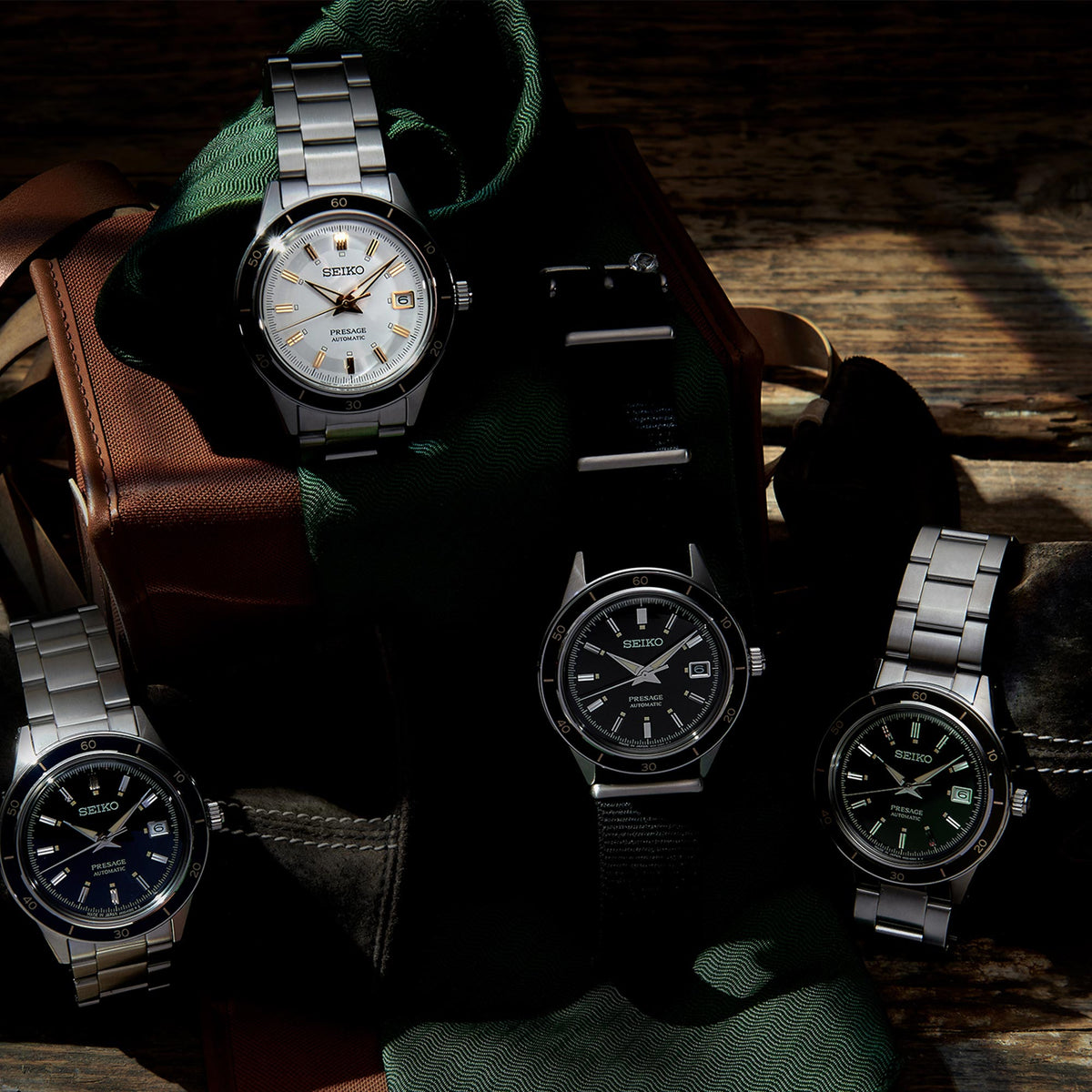 Stainless steel wristwatch with black dial on dark cushion beside other watches