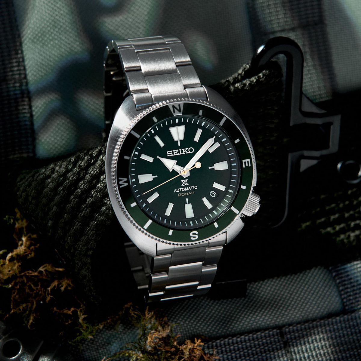 Men's steel automatic watch, green dial, link bracelet, angled view on dark fabric