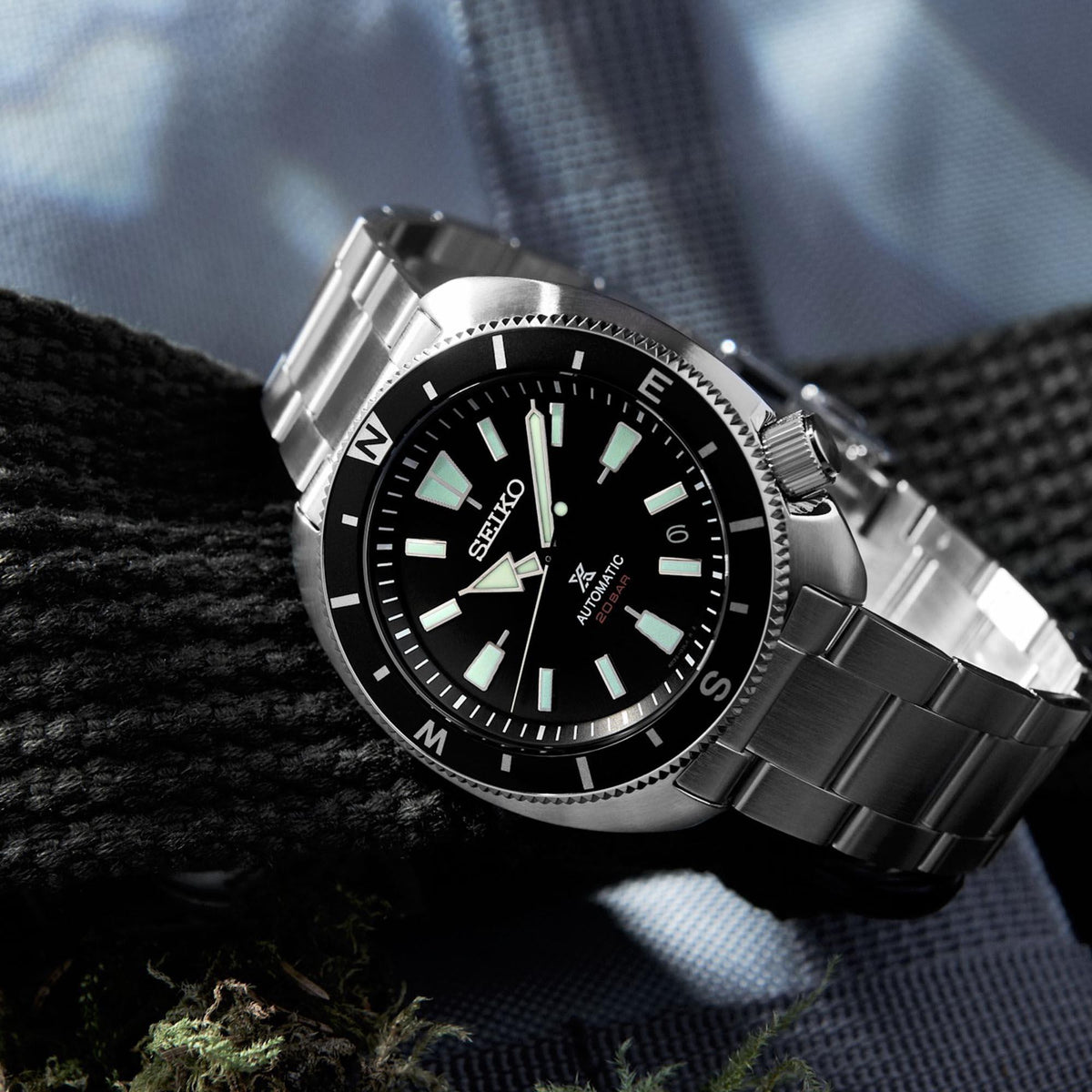 Men's stainless steel automatic watch angled close-up with black dial and metal bracelet