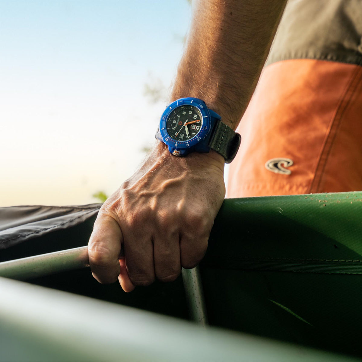 Men's Luminox watch on wrist with blue case and dark strap, black dial with orange hands