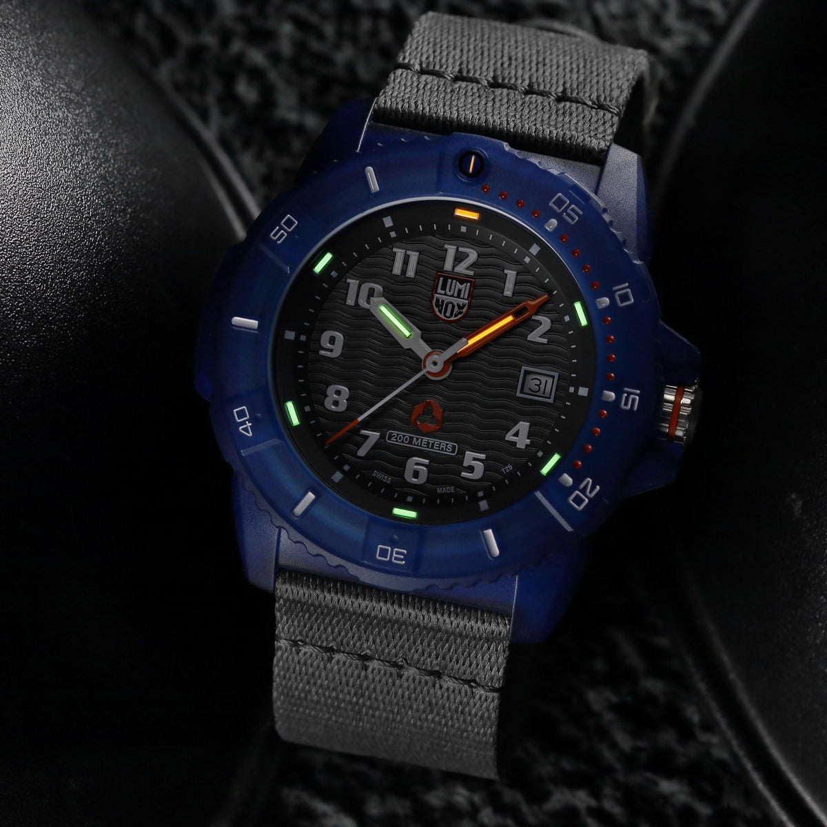 Men's quartz watch close-up: blue case, black dial with luminous green and orange hands, gray strap.