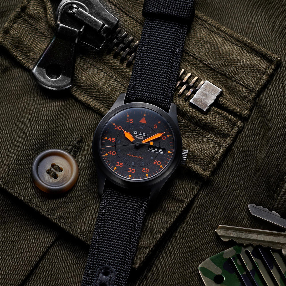 Men's automatic pilot watch with black-orange dial and black strap on dark green jacket