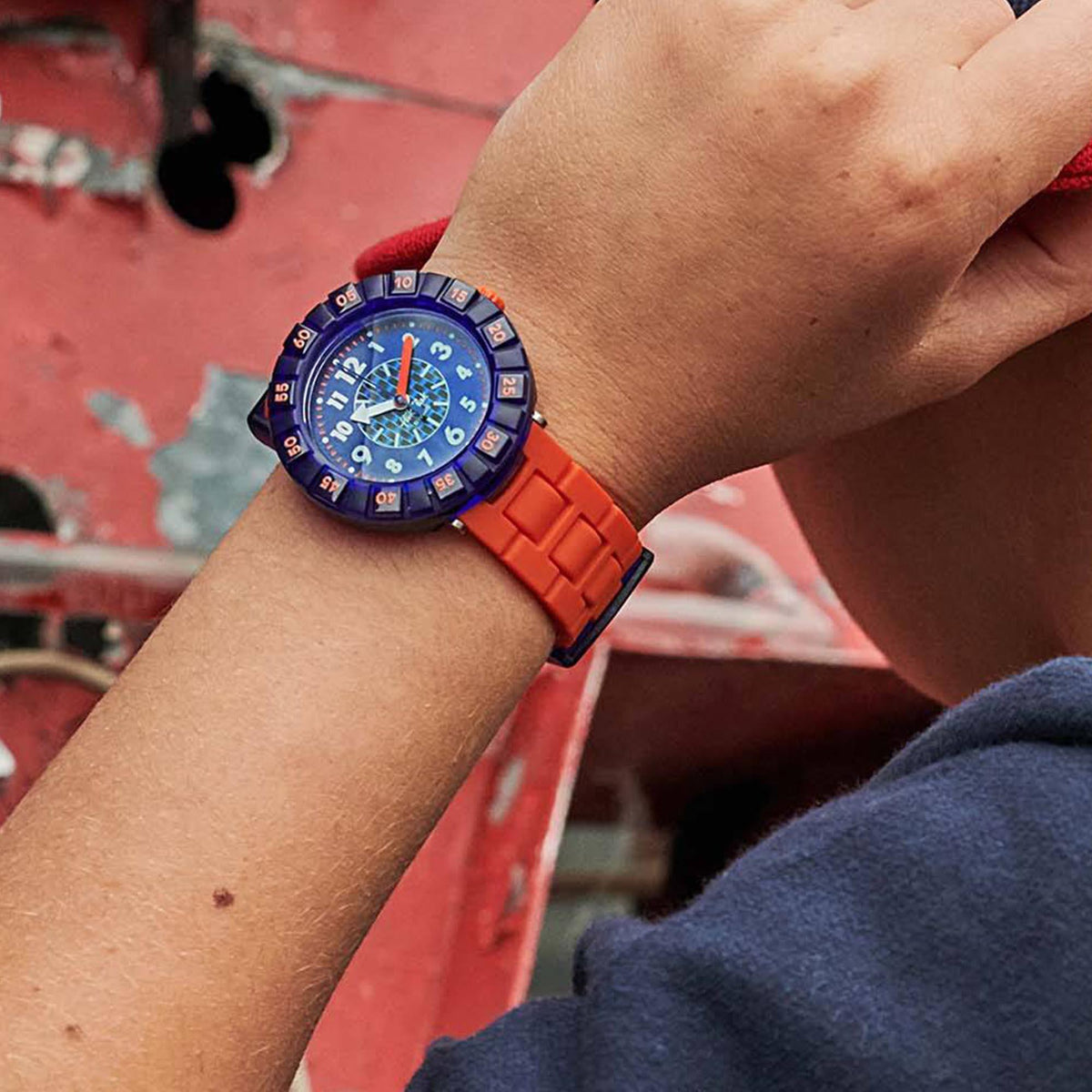 Children's wristwatch worn on arm, orange silicone strap and dark blue dial