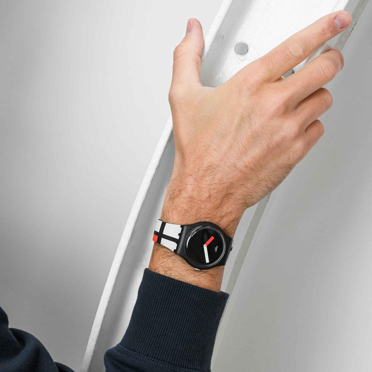 Quartz wristwatch on a wrist with black dial and red/white hands, geometric black/white strap