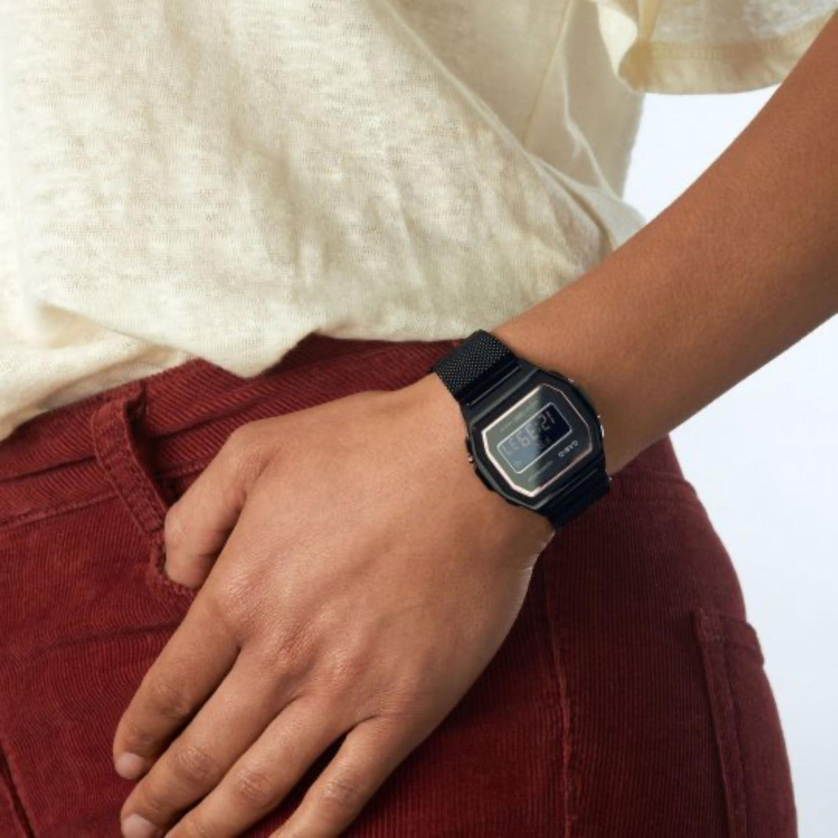 Black digital watch worn on wrist with Milanese mesh strap and square display