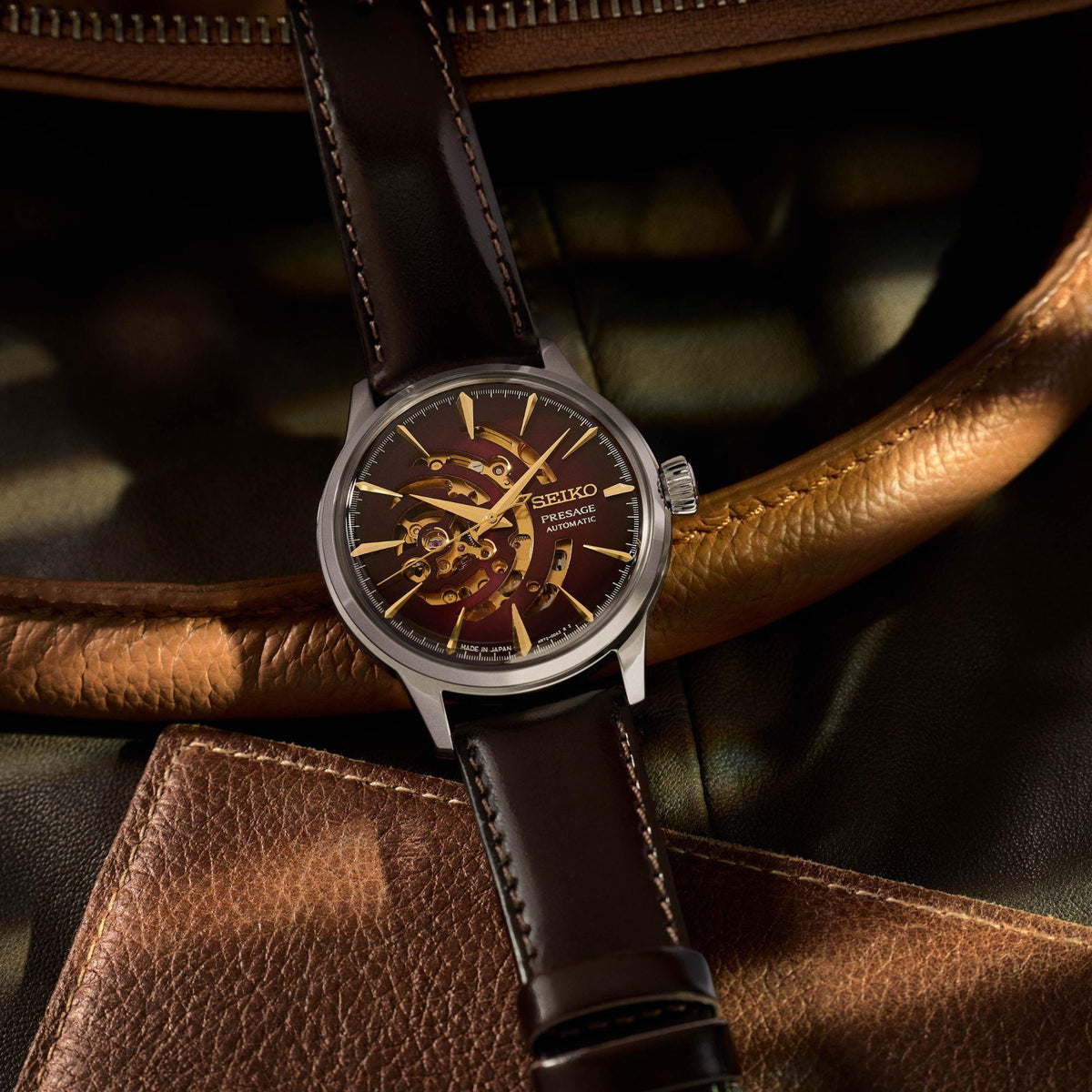 Men's automatic watch with red dial on black leather strap, gold-tone skeleton movement.