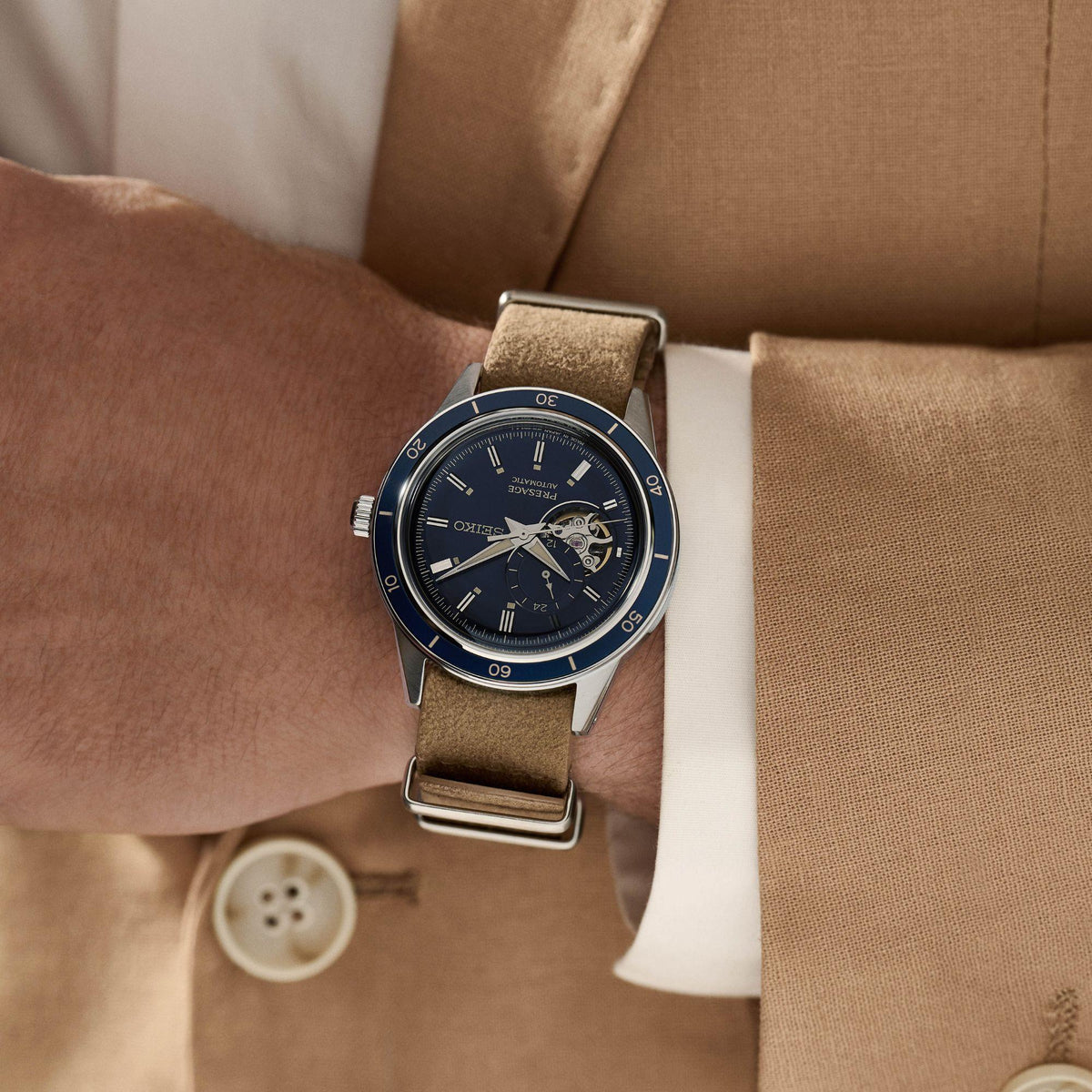 Blue dial automatic watch with beige leather strap and metal bezel on wrist