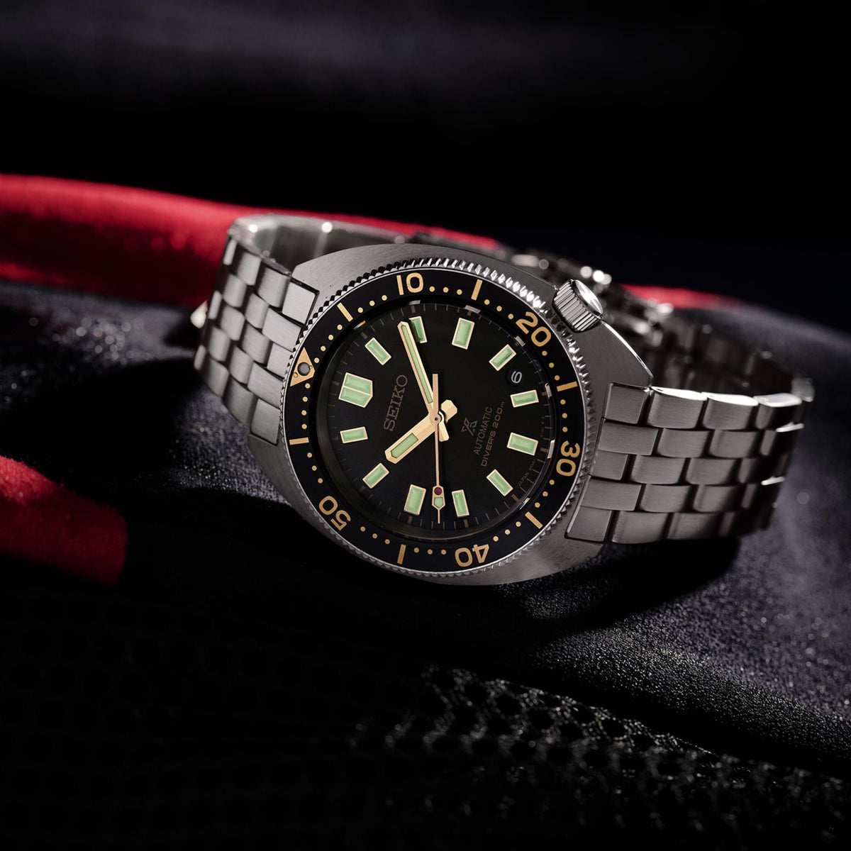 Stainless steel diver watch with green-glow indices, gold bezel, and linked bracelet