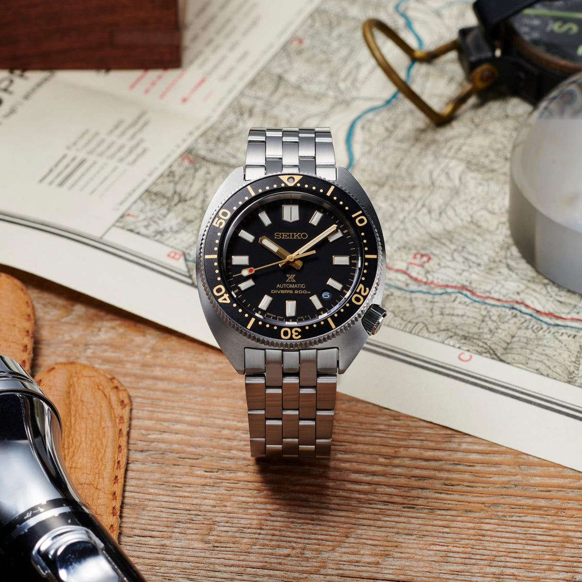 Stainless steel diver watch on surface with black dial and gold indices, linked bracelet