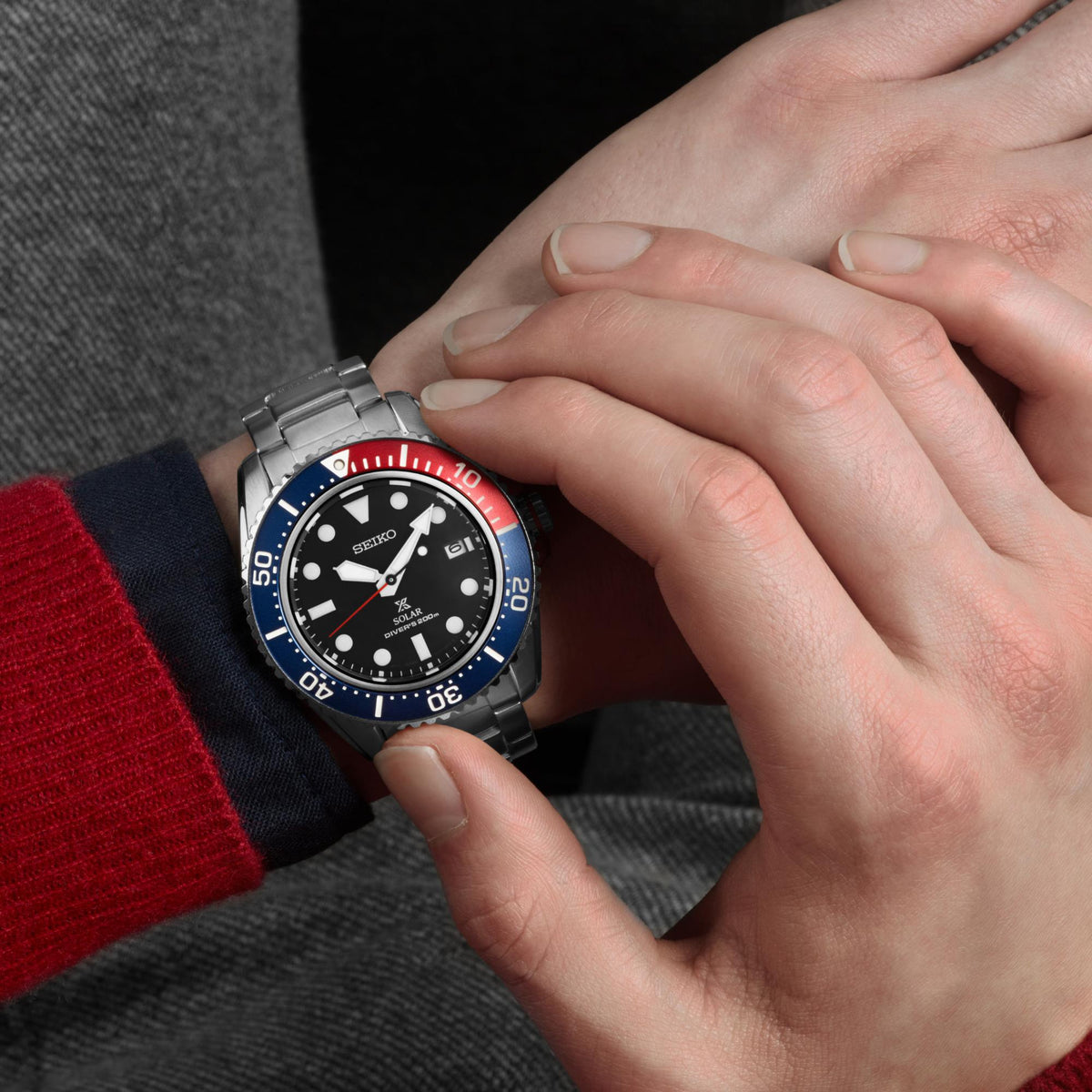 Men's stainless steel diver watch on wrist with black dial and red-blue timing bezel