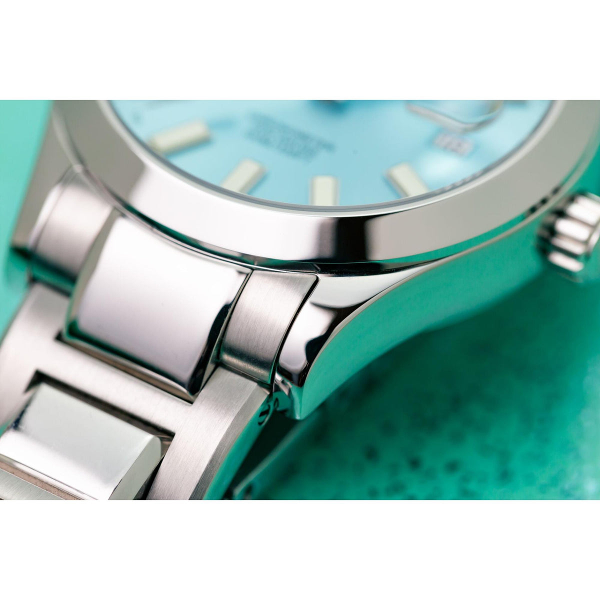 Close-up of stainless steel watch bezel over ice blue dial with bracelet links
