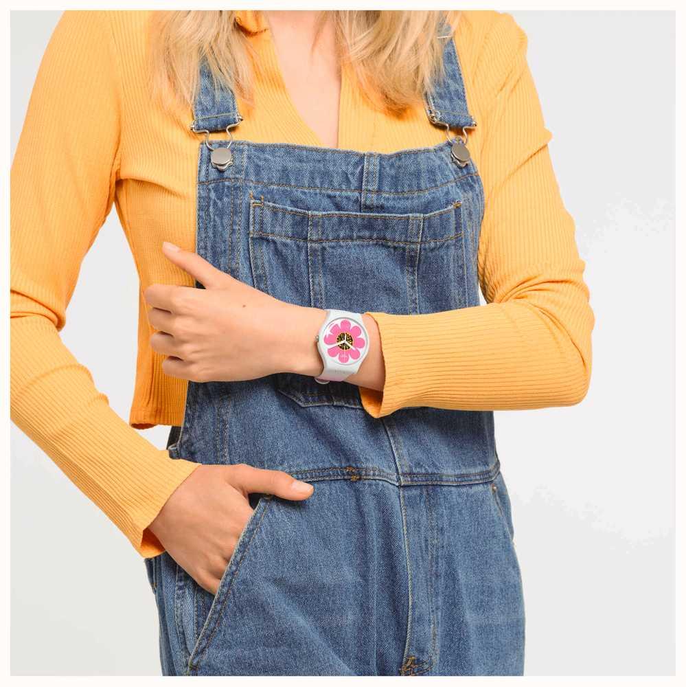 Pink flower dial silicone watch on wrist with denim overalls and orange sweater sleeves