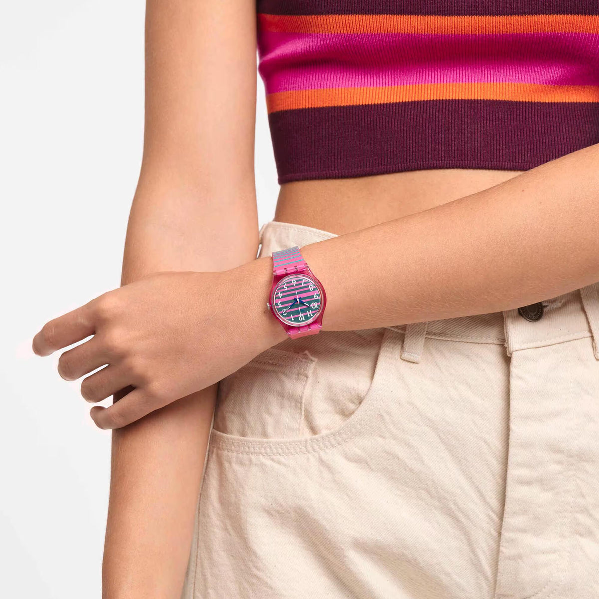 Quartz watch worn on arm with pink silicone strap and multicolor striped watch face