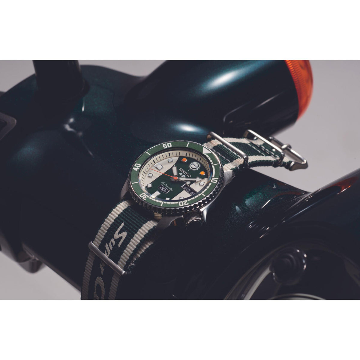 Green dial watch with striped fabric NATO strap on dark equipment