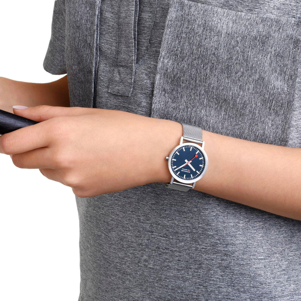 Mesh bracelet watch with deep blue dial on wrist, silver case and red hand accents