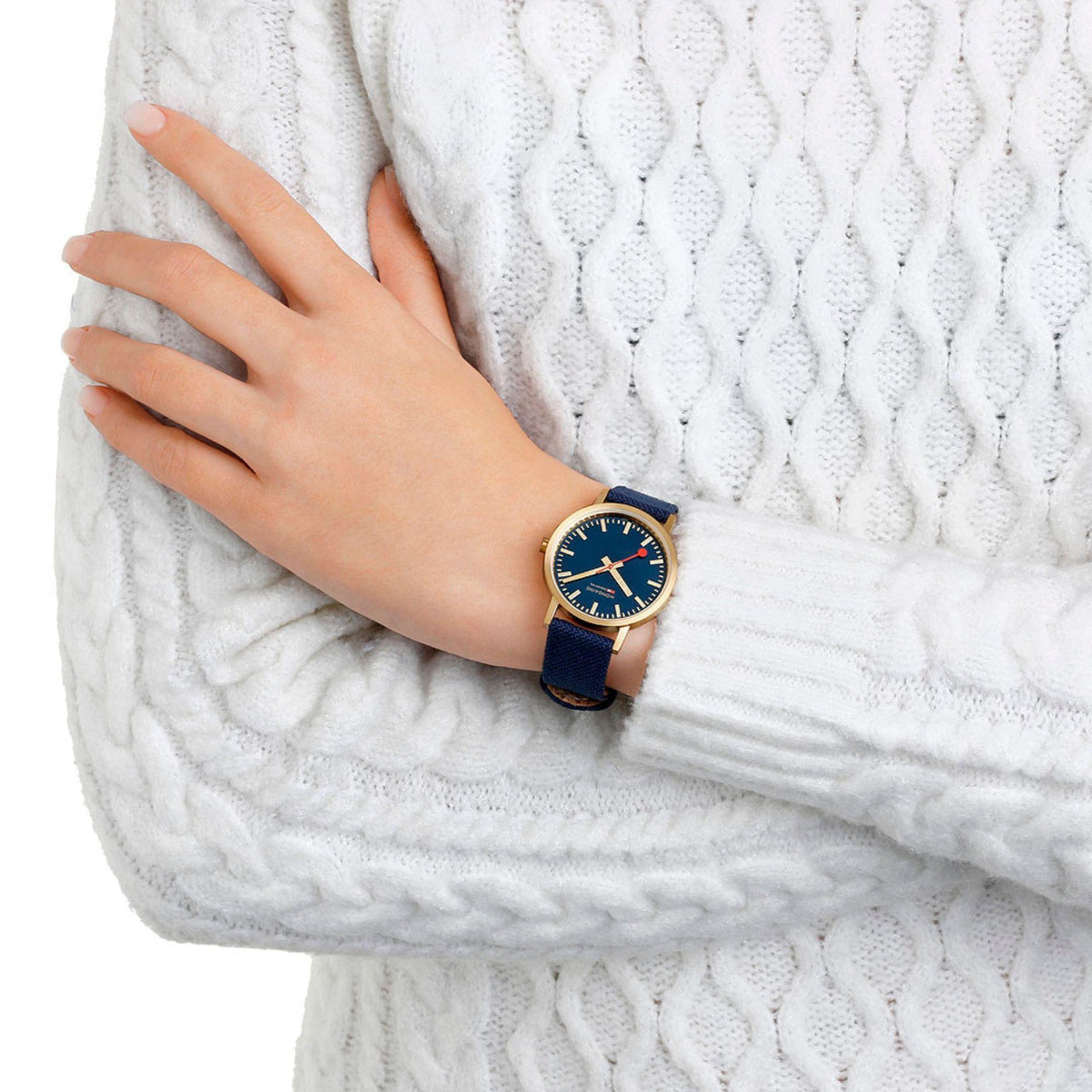 Gold-tone Mondaine watch with dark blue dial and red seconds, deep ocean blue strap on wrist.
