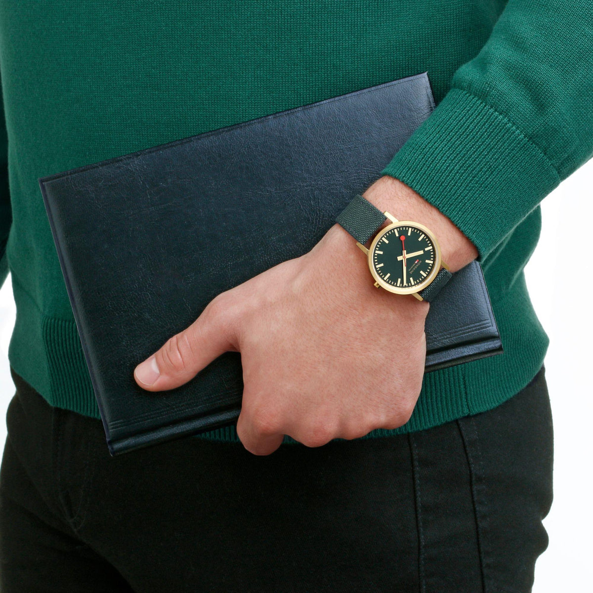 Green dial watch with gold-tone case and green fabric strap on wrist over a sweater cuff
