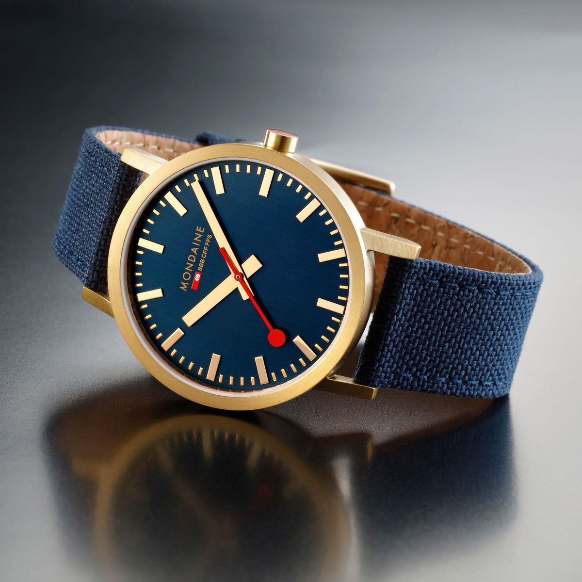 Mondaine Classic wristwatch with deep blue dial, red hands, and navy fabric strap