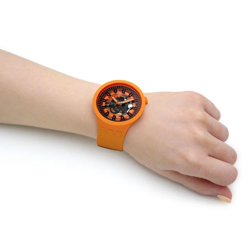 Orange skeleton dial watch with silicone strap worn on wrist