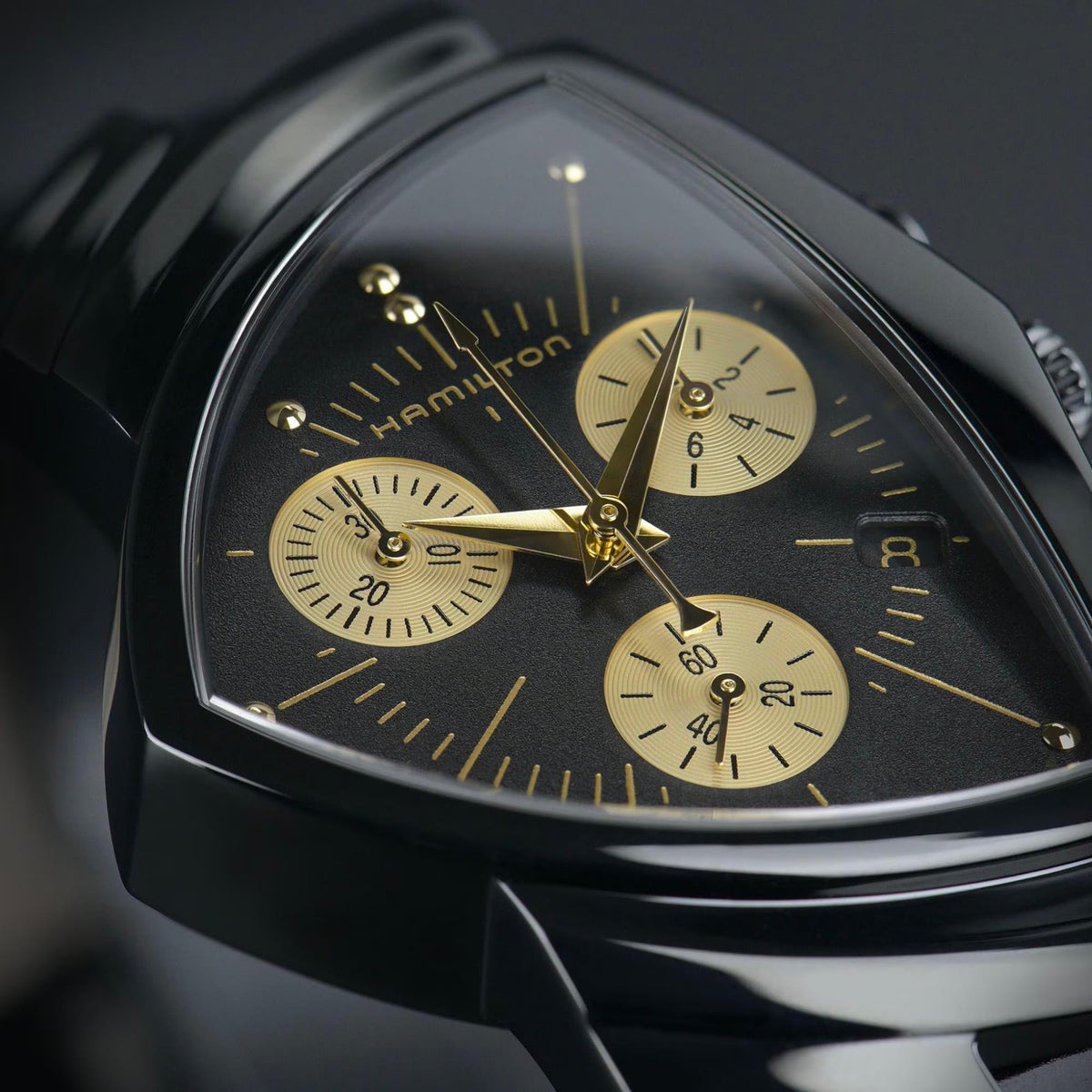 Round chronograph watch with black dial, gold subdials, and gold-tone hands