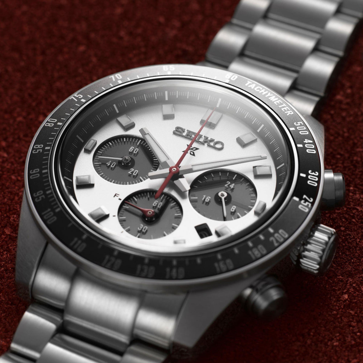 Chronograph watch close-up: silver dial with red chronograph hand, tachymeter bezel, three subdials