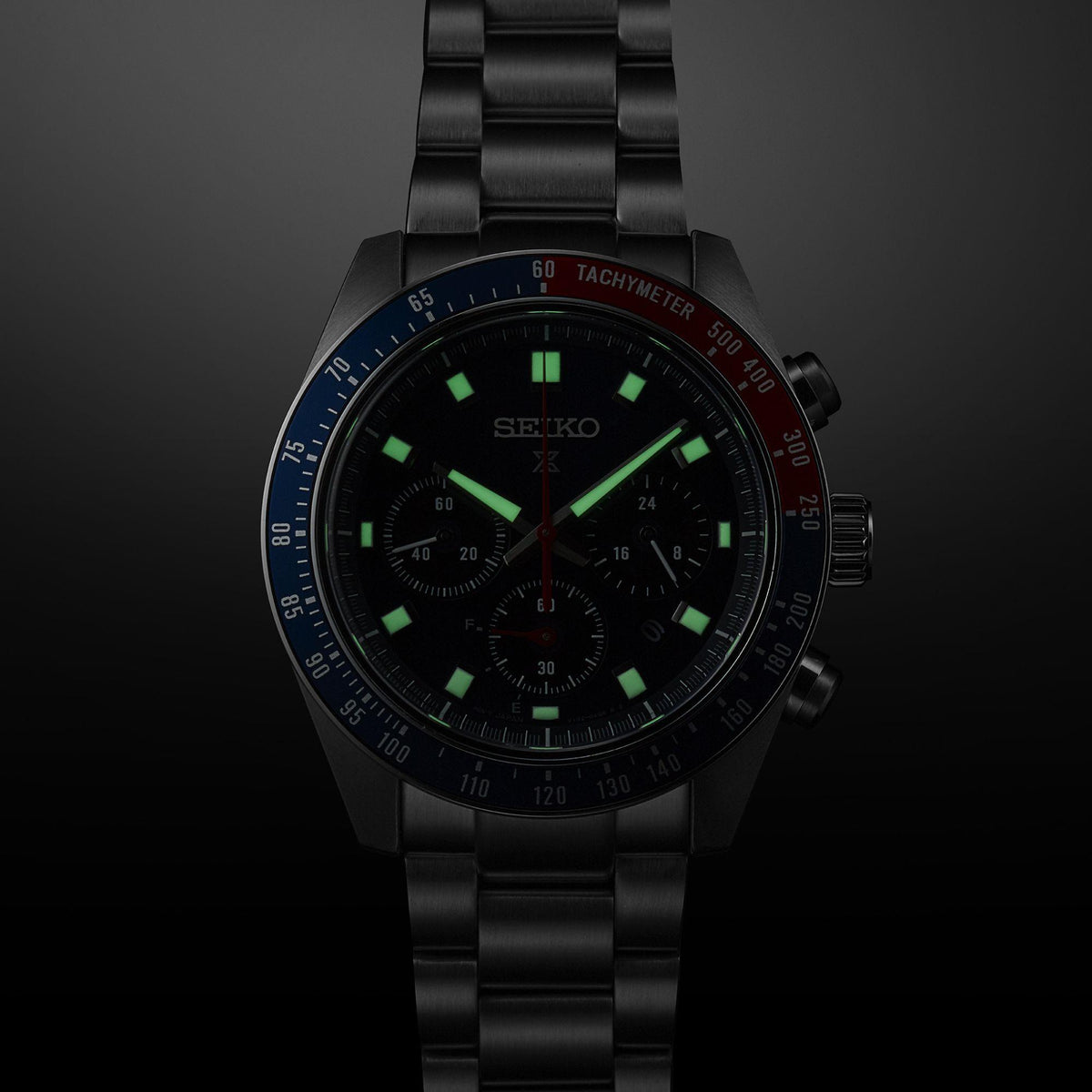 Men's chronograph watch with dark dial, green luminous markers, tachymeter bezel, steel bracelet
