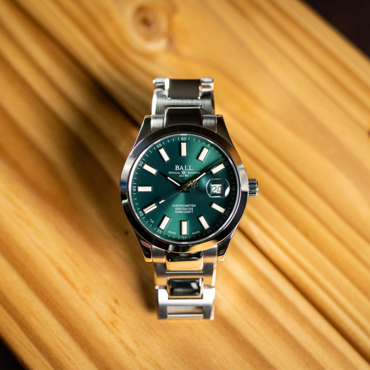 Men's wrist watch on wooden surface with dark green dial, stainless steel bracelet, date at 24.