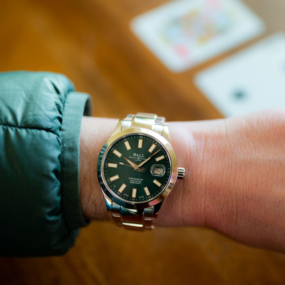 Men's wrist watch with dark green dial and stainless steel bracelet worn outdoors.