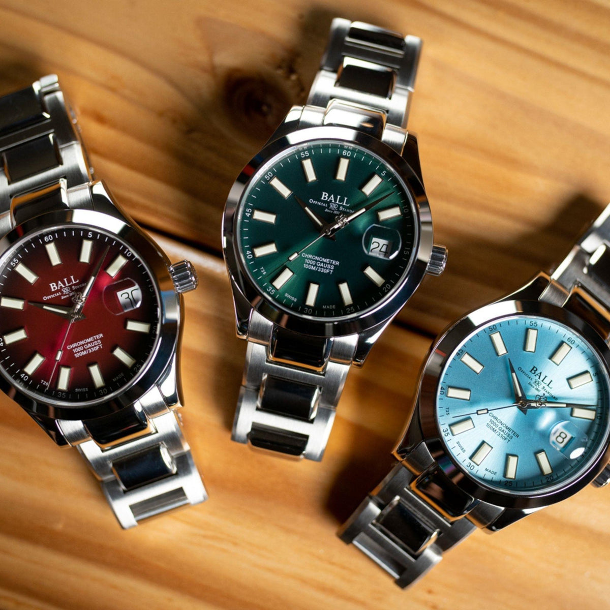 Set of men's wrist watches with stainless steel bracelets and different colored dials on wood.