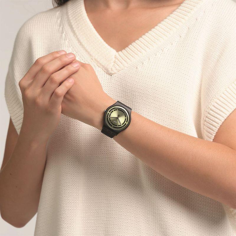 Swatch watch on wrist with olive-green dial and black silicone strap