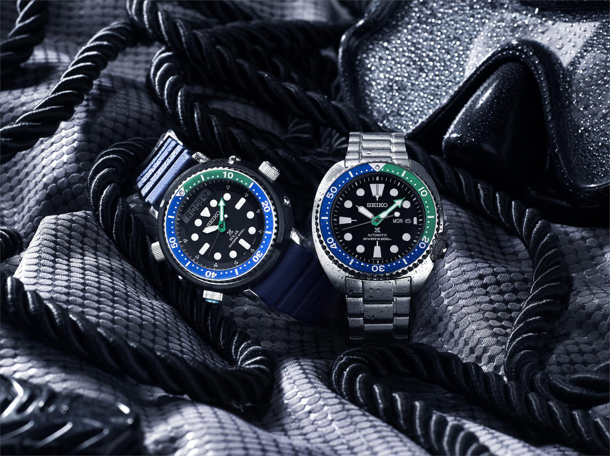 Pair of diver watches with blue bezels and green markers, black dials, stainless bracelets