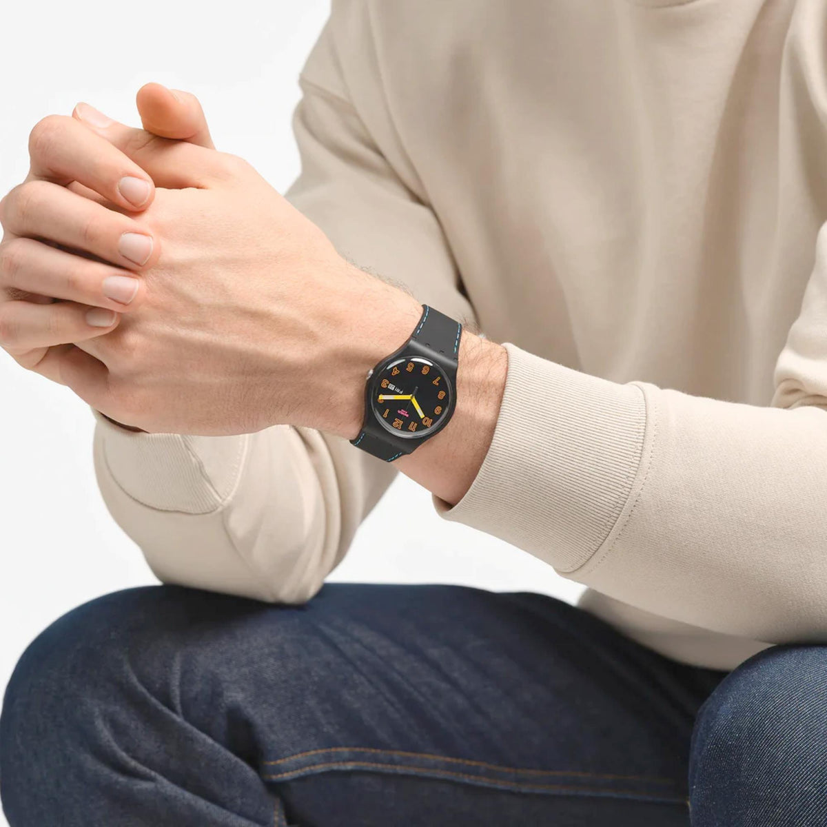 Quartz watch worn on wrist, round black dial, yellow hands, blue-stitch silicone strap