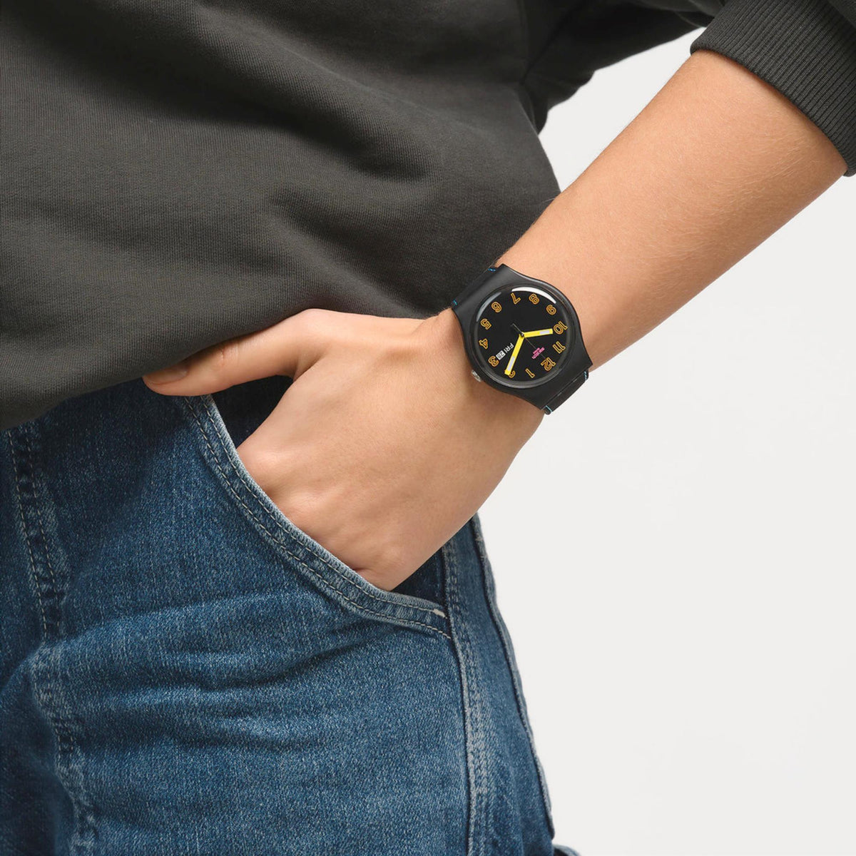 Quartz wristwatch on wrist over denim, round black dial with yellow hands and blue-stitch strap