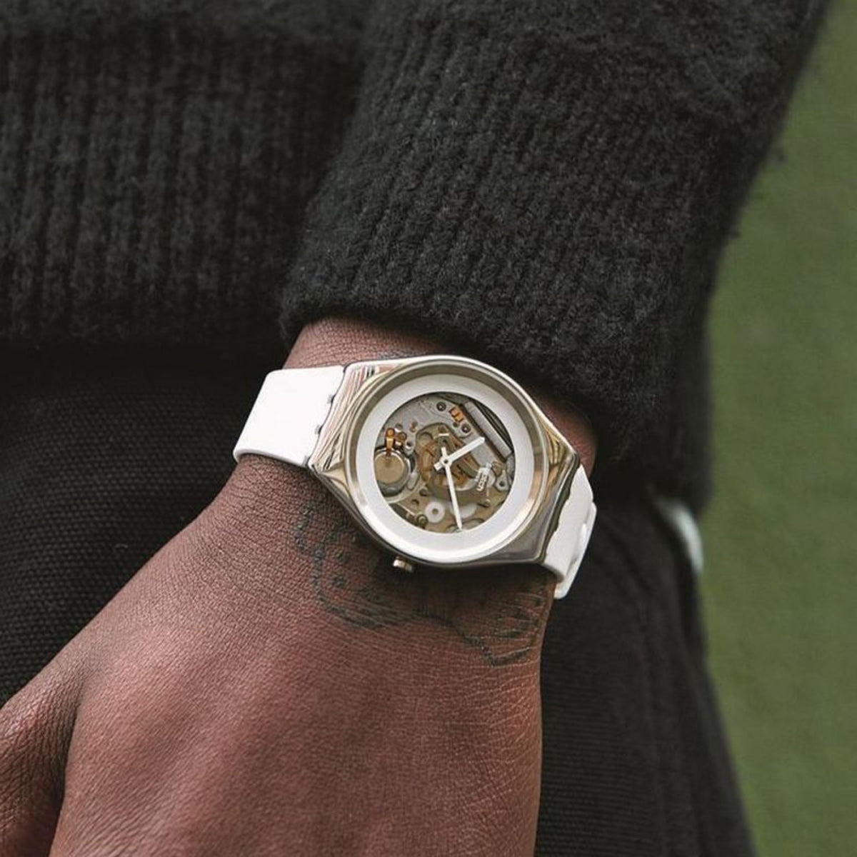 Men's wristwatch on wrist with white strap; silver case and visible watch mechanism