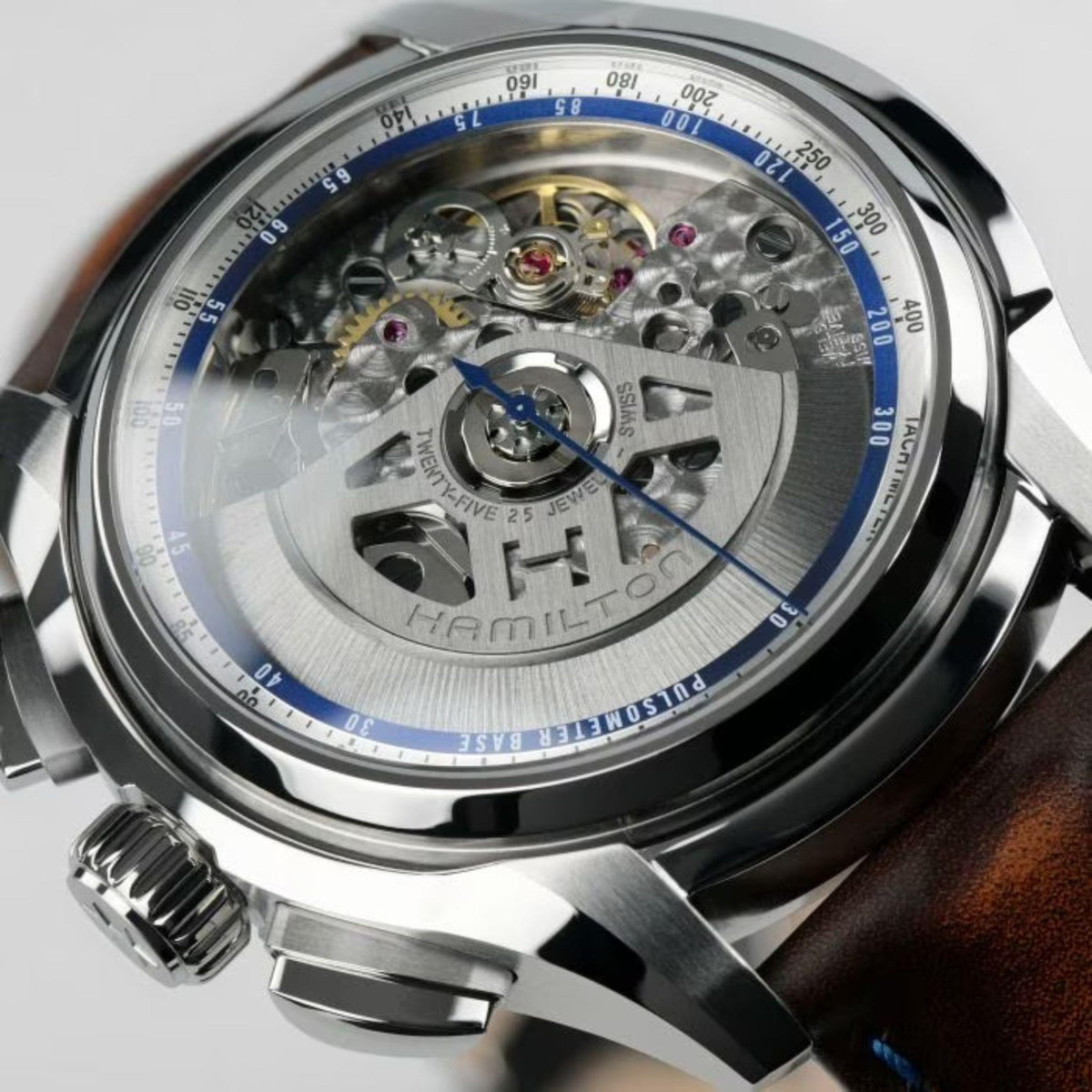Men's silver automatic watch caseback with visible movement, blue ring, and brown leather strap