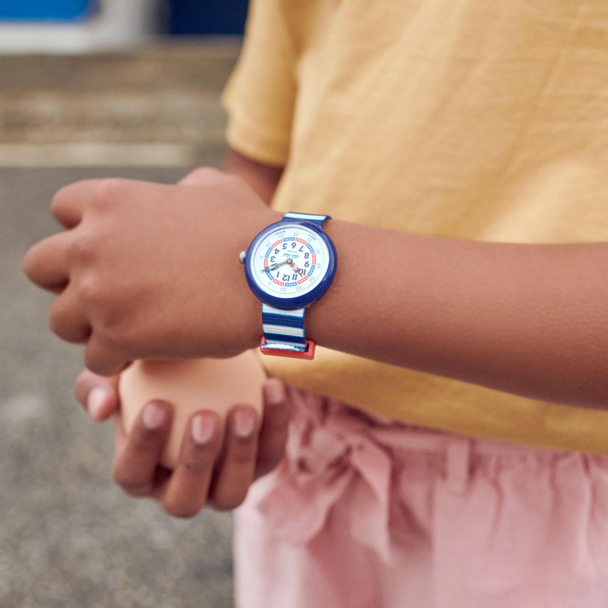 Child wearing kids watch: small round blue case, white dial, blue-and-white striped strap