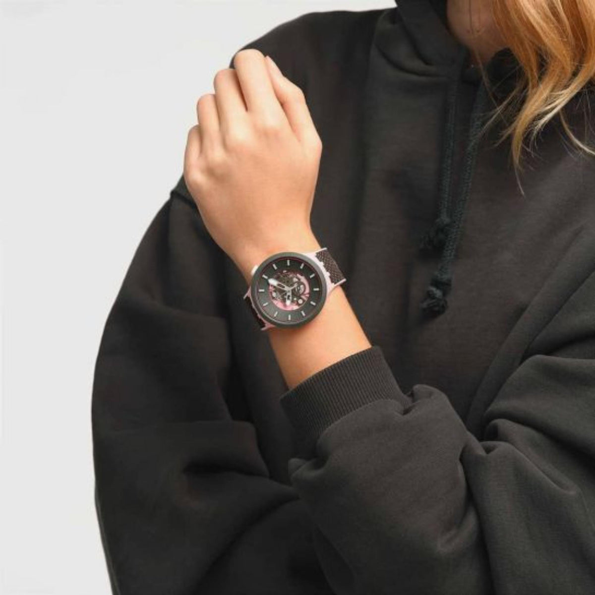 Women’s Swatch watch on wrist, round dark case, pink skeleton dial, gray strap