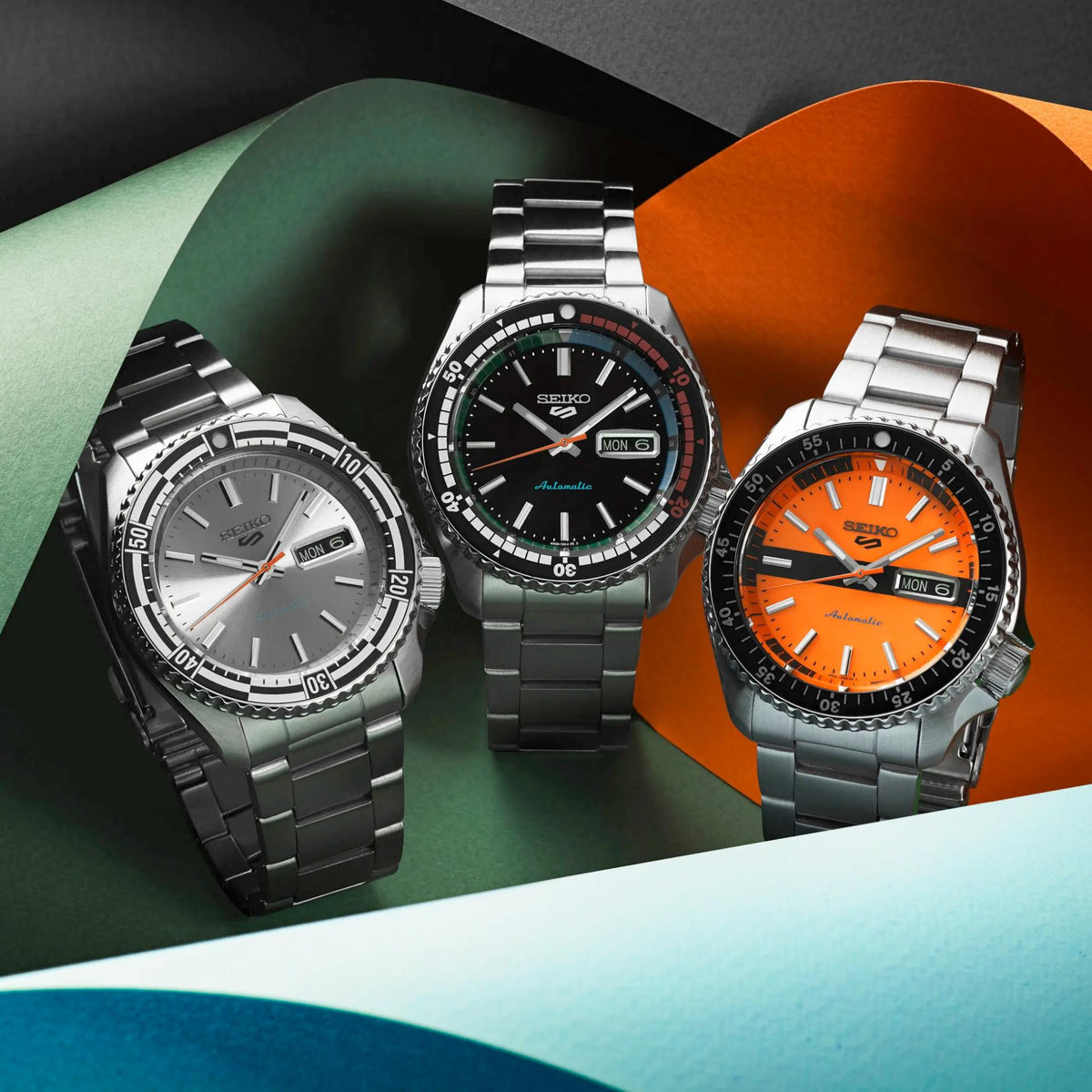 Seiko 5 Sports automatic watches: orange, black/green, and silver dials on steel bracelets