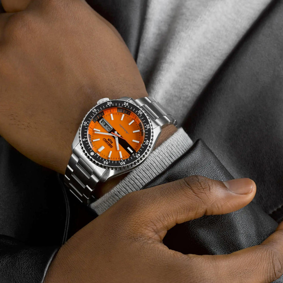 Seiko sports watch on wrist, close-up orange dial and steel bracelet links.