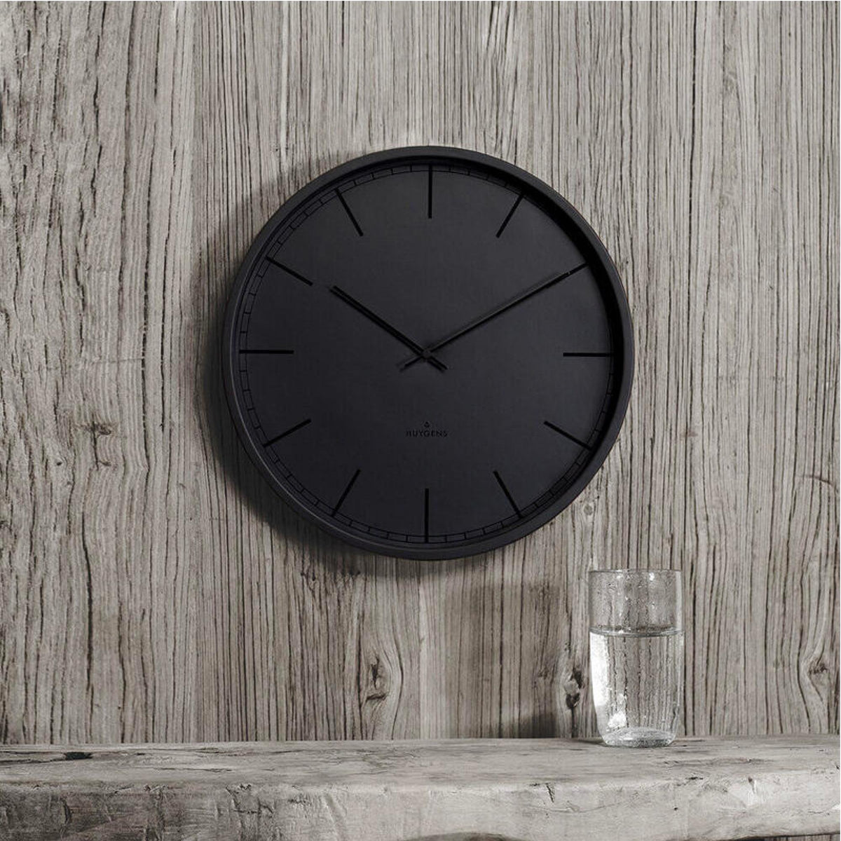 Black round wall clock with three hands and hour index marks, wall-mounted