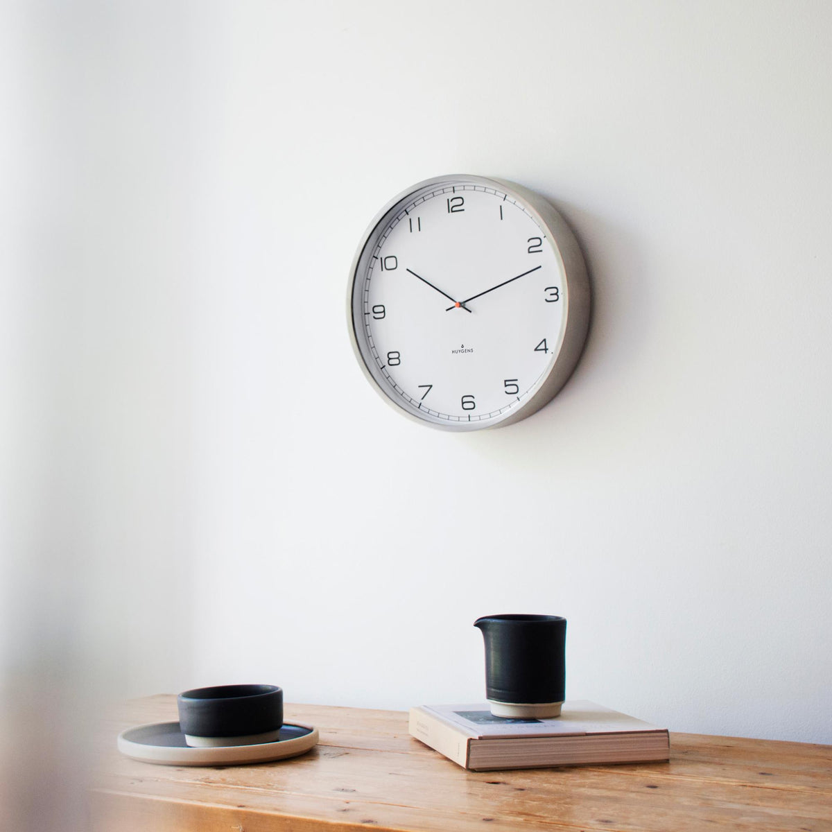 Huygens wall clock centered on wall, white dial with black hour marks and red second dot
