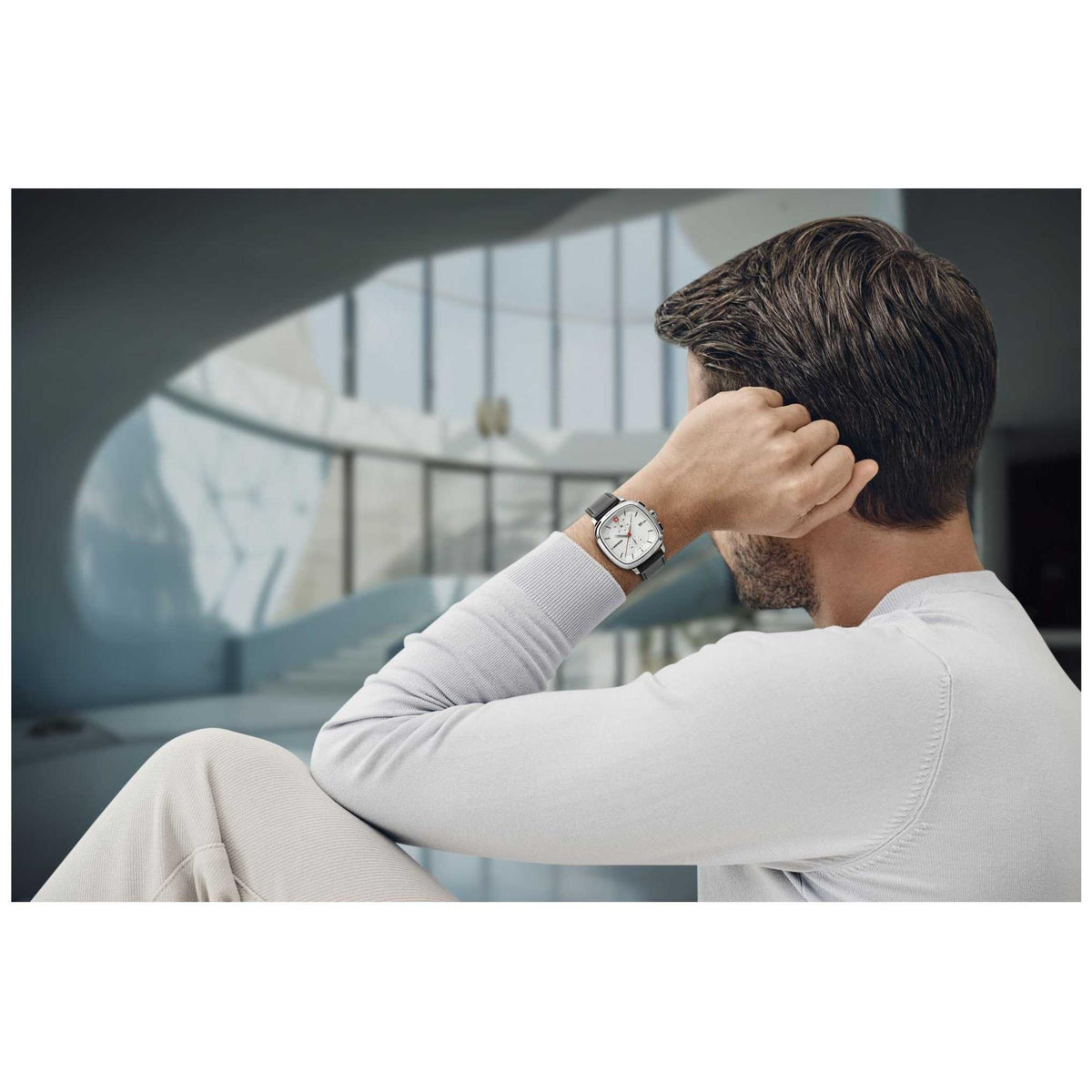 Silver chronograph watch with black leather strap on man's wrist in outdoor setting.