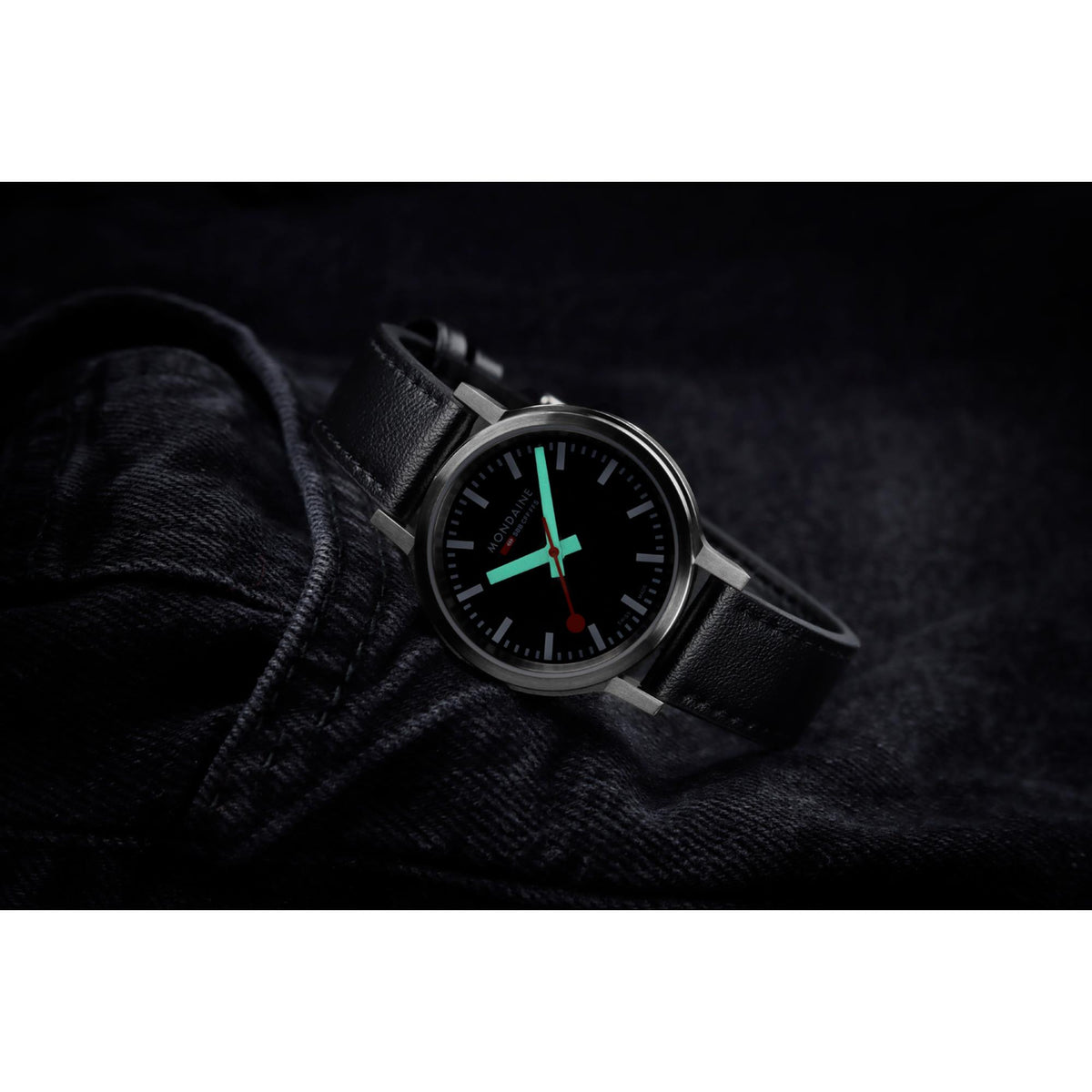 Black dial quartz watch with black leather strap and silver-tone case on dark denim