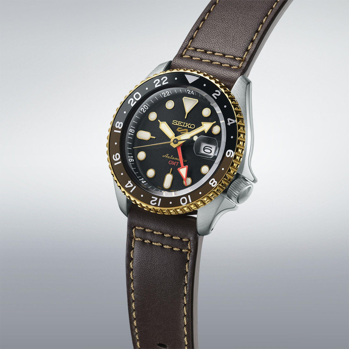 GMT watch in profile with black dial and gold bezel, worn on brown leather strap.