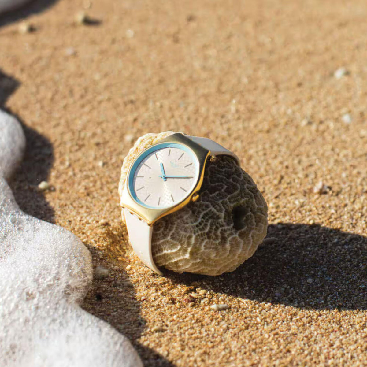 Ivory silicone watch with gold-tone bezel and light blue hands on a rocky close-up