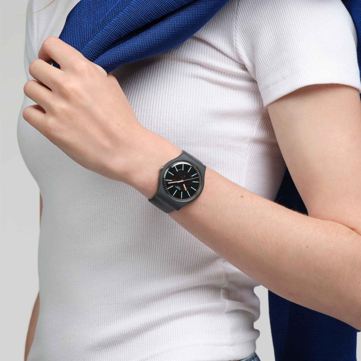 Swatch men's quartz watch on wrist, dark gray silicone strap, black dial with blue markers